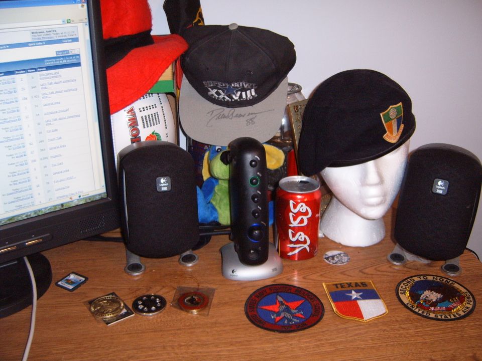 Desk with computer monitor displaying a spreadsheet, two black speakers, a red Coca-Cola can, and several hats