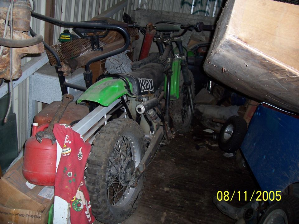 Green dirt bike with KDX markings on the side, parked indoors with other items