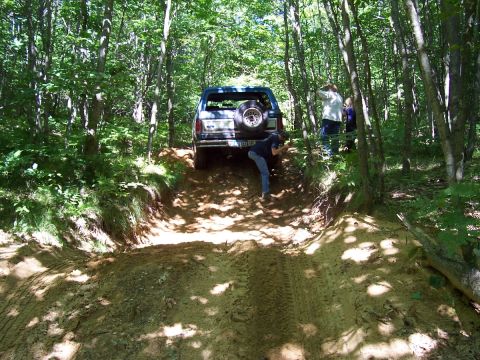 1982 Ford Bronco - A group of people are off-roading with a Ford Bronco in a wooded area.