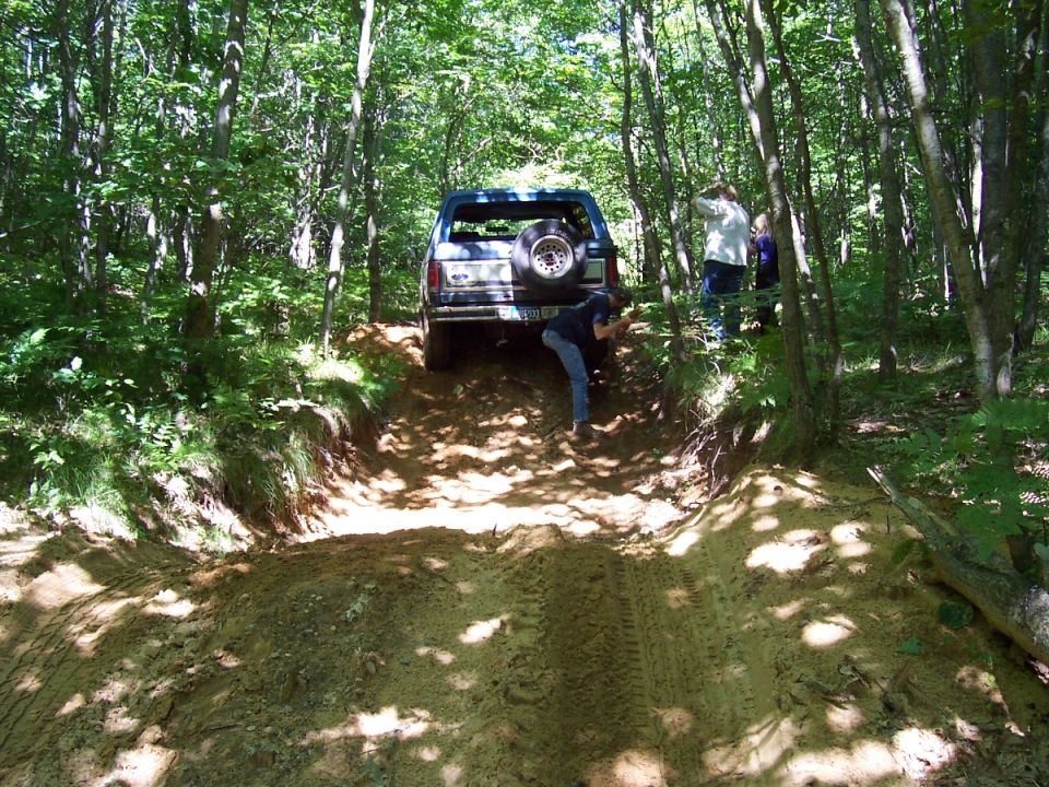 Ford Bronco climbing a dirt hill in a forest. Someone is pushing on the back