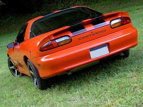 Orange fourth-gen Camaro coupe rear three-quarter view with black stripes and dark wheels on grass