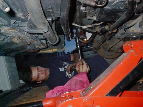 1985 Mercury Grand Marquis - A mechanic works on the underside of a vehicle, using a socket wrench.
