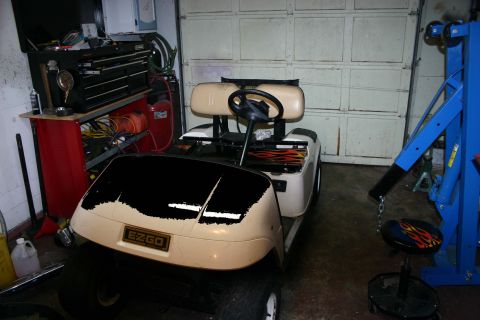 1989 Ford Bronco - EZGO golf cart with flame decals is parked in a garage next to a blue engine hoist.