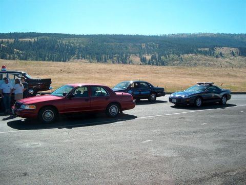 2001 Ford Crown Victoria - A red 2001 Ford Crown Victoria is parked alongside other vehicles under a clear blue sky.