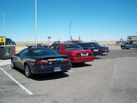 2001 Ford Crown Victoria - A variety of law enforcement vehicles are parked in a lot, with a truck and camper visible in the background.