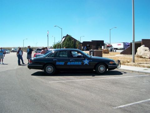 2001 Ford Crown Victoria - A black 2001 Ford Crown Victoria police car, marked 'Town Marshal', is parked in a lot on a sunny day.
