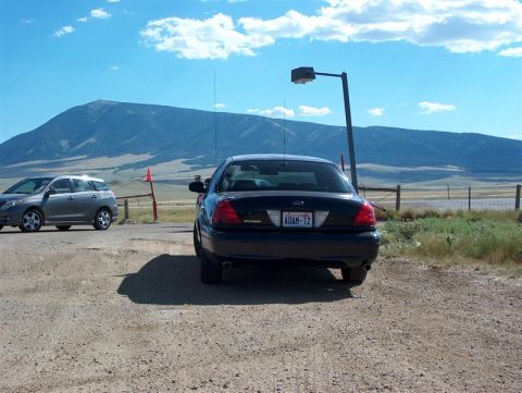 2001 Ford Crown Victoria - A black 2001 Ford Crown Victoria is parked on a dirt lot with another vehicle, set against a backdrop of mountains under a blue sky.