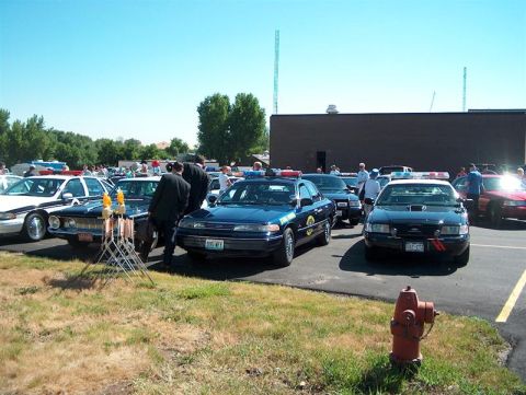2001 Ford Crown Victoria - A gathering of police vehicles, possibly at a car show or conference, under a clear blue sky.