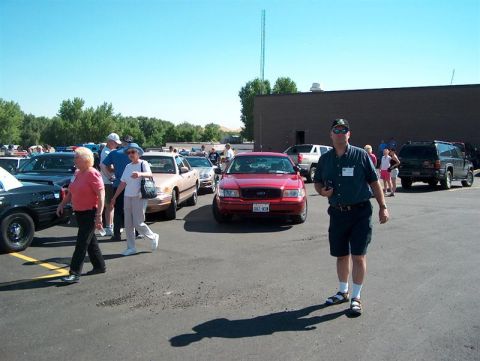 2001 Ford Crown Victoria - A red 2001 Ford Crown Victoria is seen from the front in a parking lot with other vehicles and people.