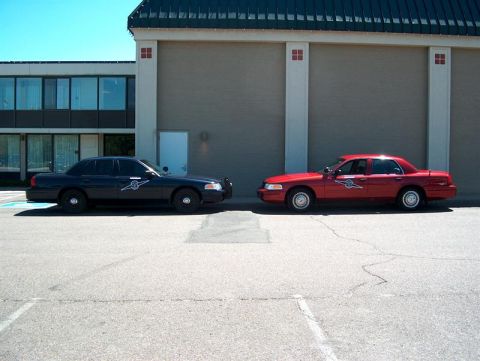 2001 Ford Crown Victoria - Two Ford Crown Victoria police cars, one black and one red, are parked next to each other.