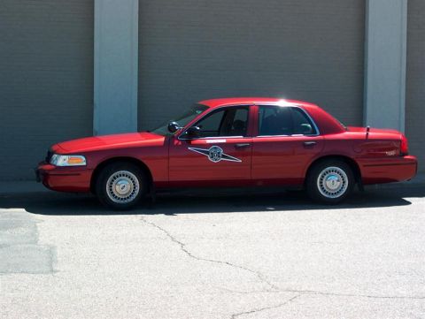 2001 Ford Crown Victoria - A red sedan with a circular emblem on the door is parked outside a building.