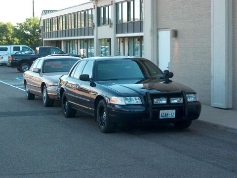 2001 Ford Crown Victoria - A black 2001 Ford Crown Victoria police car is parked in front of a building, with another car behind it.