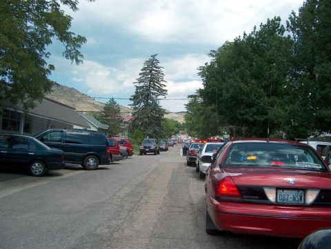 2001 Ford Crown Victoria - A line of vehicles, including a red 2001 Ford Crown Victoria, parked on a street with trees and hills in the background.