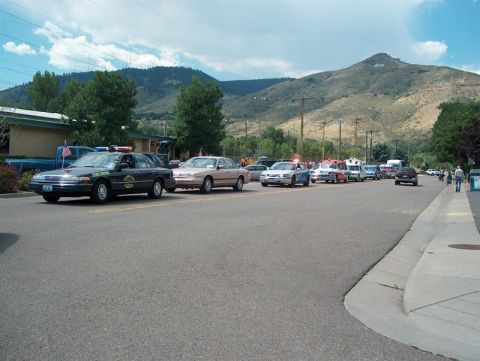 2001 Ford Crown Victoria - A line of vehicles, including what appears to be a police car, are parked on a street with a mountain range in the distance.