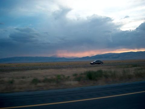 2001 Ford Crown Victoria - A lone sedan travels a highway at dusk, with a dramatic sky and distant mountains.