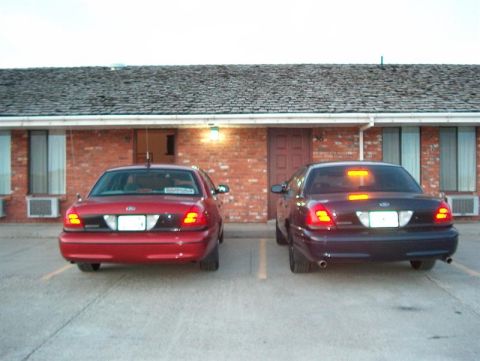 2001 Ford Crown Victoria - Two Ford Crown Victorias are parked outside a brick building with a shingled roof.