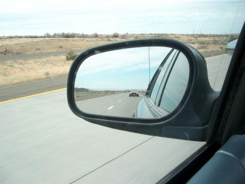 2001 Ford Crown Victoria - A red car is visible in the side mirror while driving on a highway through a desert landscape.