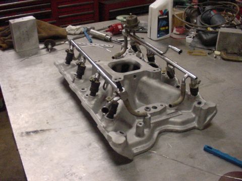 1969 Ford Bronco - A close-up view of an aftermarket fuel injection intake manifold assembly, likely for a V8 engine, resting on a metal surface.