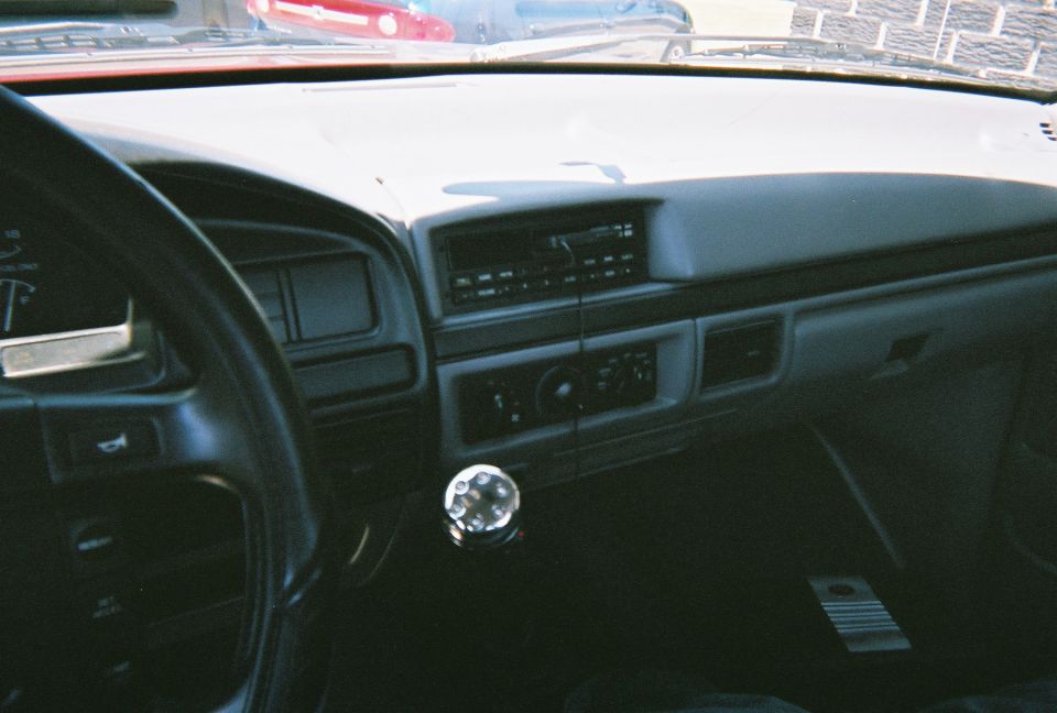 Gray dashboard interior of 1996 Ford F-150 with steering wheel, radio, and chrome floor shifter knob