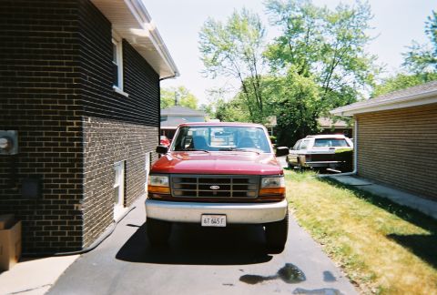 1996 Ford F-150 - A red Ford truck is parked in a driveway next to a brick house and a garage.