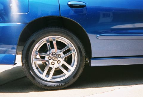 1996 Ford F-150 - Close-up of a blue car's rear wheel and fender, showing a Chevrolet emblem on the wheel.