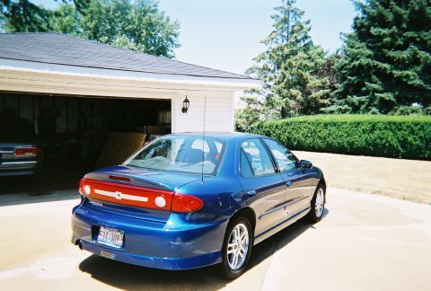 1996 Ford F-150 - A blue sedan is parked outside a residential garage, with another vehicle partially visible inside.