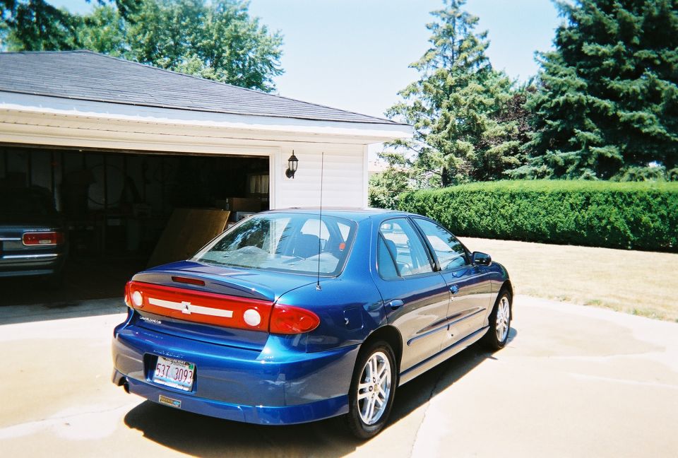 Blue sedan parked in driveway next to an open garage. Another car is visible inside the garage