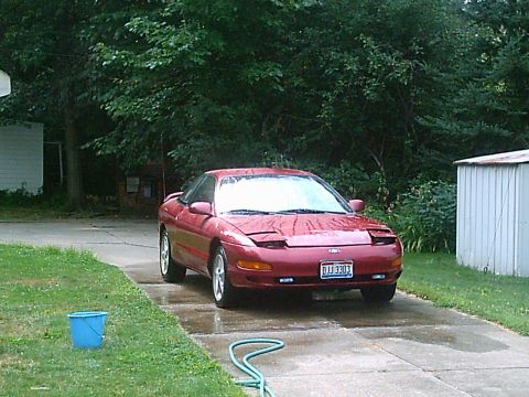 1993 Ford Probe - A red 1993 Ford Probe is parked on a wet driveway with trees and a shed in the background.
