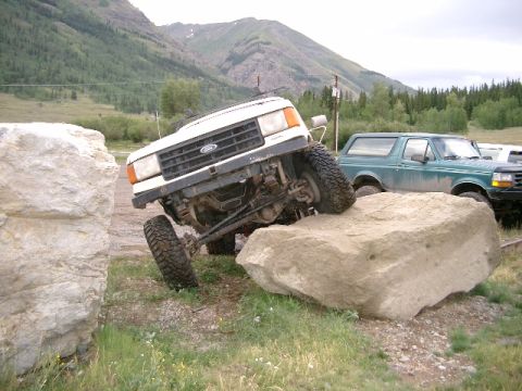 1987 Ford Bronco - White 1987 Ford Bronco navigates a large boulder obstacle, with another Bronco visible behind it.
