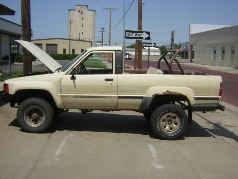 1995 Ford Bronco - This cream-colored pickup truck is viewed from the side with its hood open. A roll cage is visible in the bed.