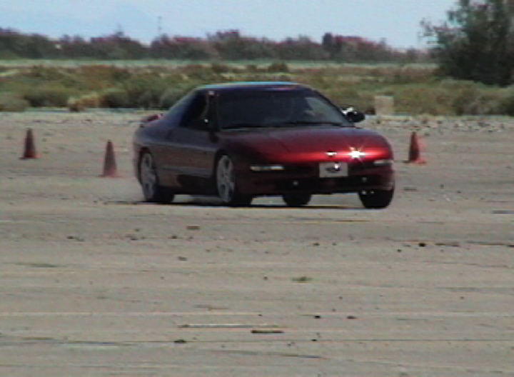Red 1996 Ford Probe driving on a dirt track with orange cones
