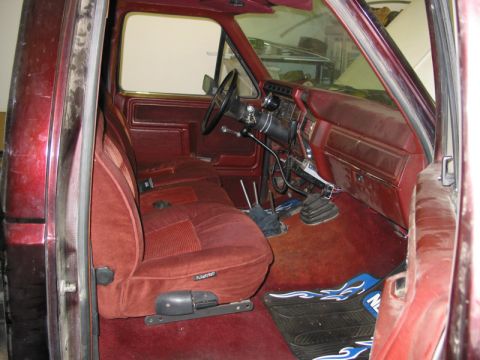 1981 Ford Bronco - The interior of a red truck shows its maroon seats, dashboard, and floor mats, with a watermark at the bottom.