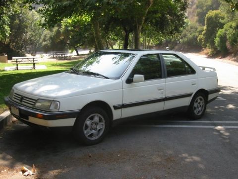 1989 Peugeot 405 - White 1989 Peugeot 405 sedan parked in a shaded outdoor area with trees and picnic tables.