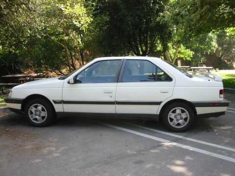 1989 Peugeot 405 - A white 1989 Peugeot 405 sedan is parked in a lot with trees and picnic tables in the background.