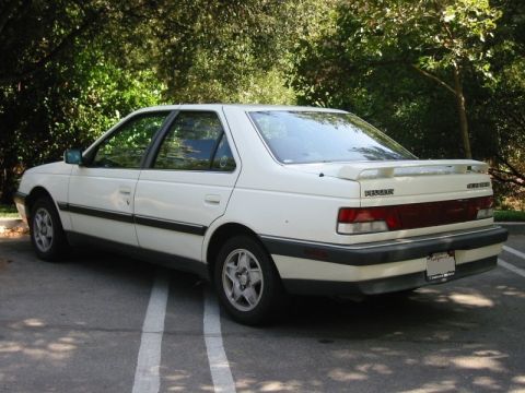 1989 Peugeot 405 - This white 1989 Peugeot 405 sedan is viewed from the rear 3/4 angle, showing its spoiler and license plate.