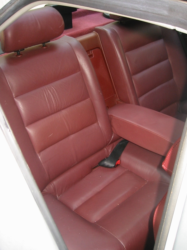 Burgundy leather rear bench seat inside a car with black seatbelt visible