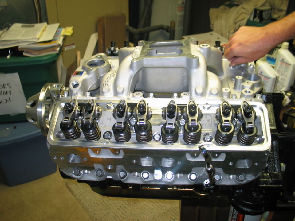 Engine block with polished valve covers and intake manifold, a hand is adjusting a bolt