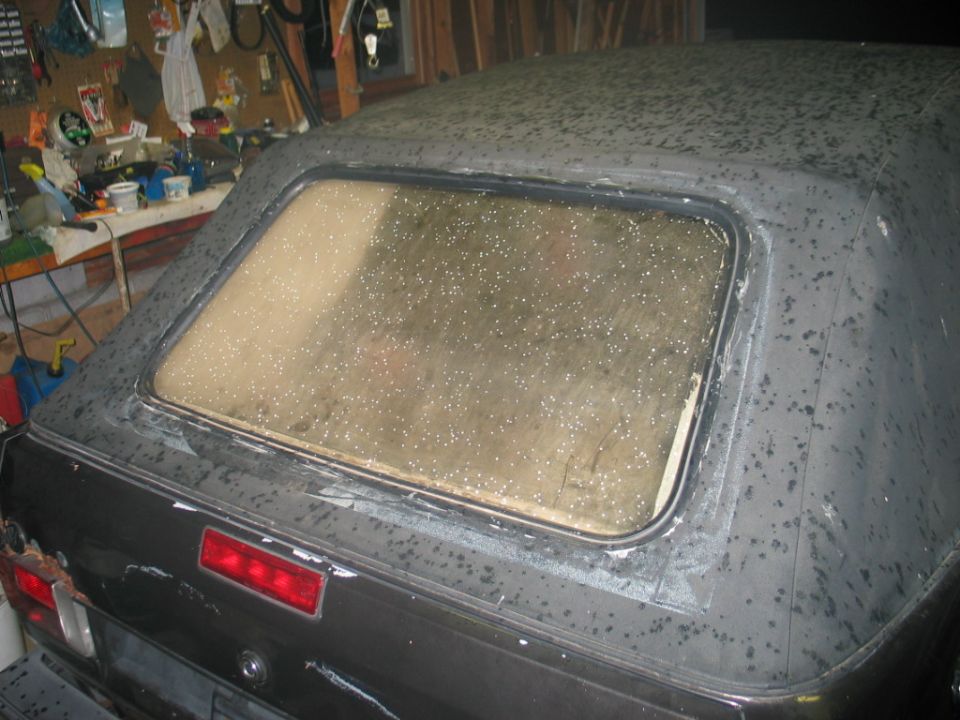 Weathered black convertible top with hazy rear window and sealant residue during repair in a garage