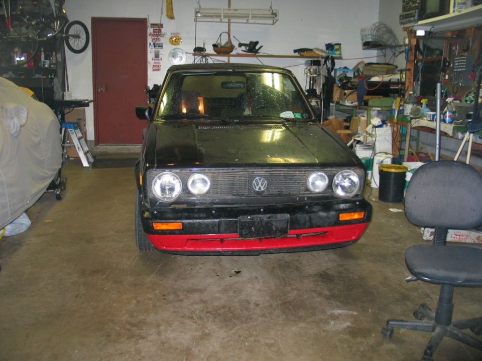 Front of black VW Cabriolet with red lower bumper in a garage