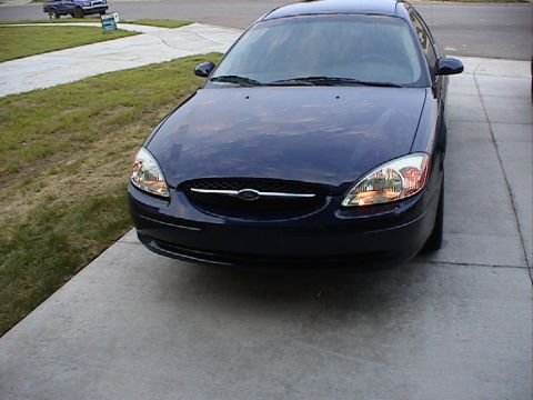 2000 Ford Taurus - A dark blue sedan is parked in a driveway, facing the camera. The car's grille and headlights are visible.