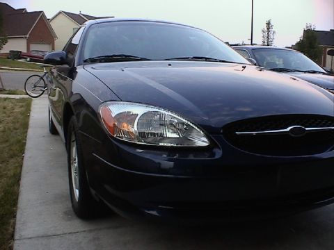 2000 Ford Taurus - Front 3/4 view of a dark blue 2000 Ford Taurus parked on a driveway. Another vehicle is visible in the background.