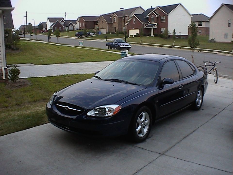 Dark blue sedan parked in driveway with houses in background. Bicycle on rack behind it