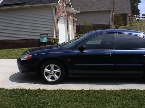 2000 Ford Taurus - Side profile of a dark blue 2000 Ford Taurus sedan parked in front of a residential garage.