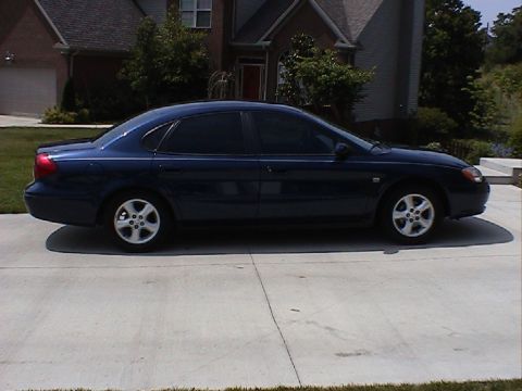 2000 Ford Taurus - A dark blue sedan is parked in front of a suburban house on a sunny day.