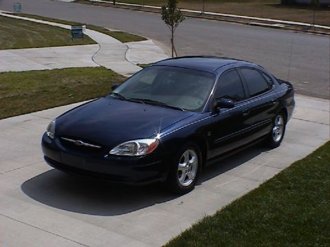 2000 Ford Taurus - This dark blue sedan, identified as a 2000 Ford Taurus, is shown parked on a residential driveway.