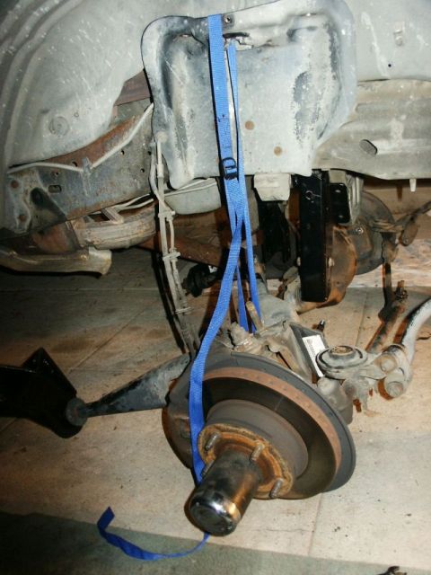 1996 Ford Bronco - Close-up of a vehicle's suspension system, showing the brake rotor and hub assembly secured by a blue strap.