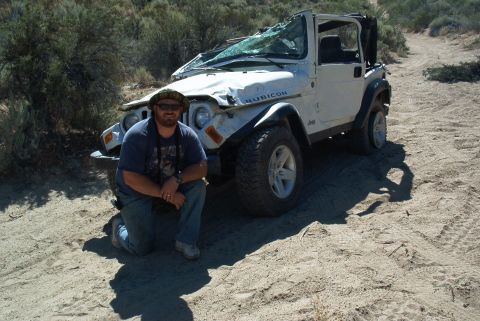 1986 Ford Bronco - A man kneels in front of a white Jeep Wrangler Rubicon that has sustained significant damage to its windshield and hood.