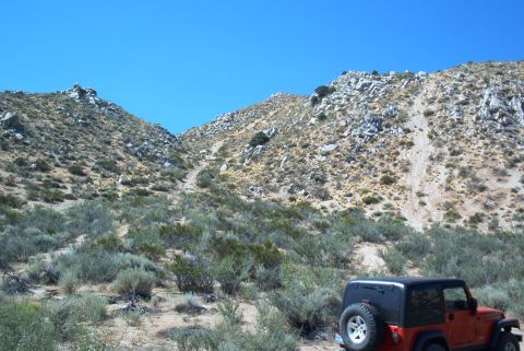 1986 Ford Bronco - A Jeep Wrangler is parked in a dry, hilly terrain under a bright blue sky.