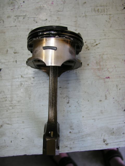 1996 Ford Probe - A piston and connecting rod assembly, likely from an engine rebuild, rests on a workbench surface.