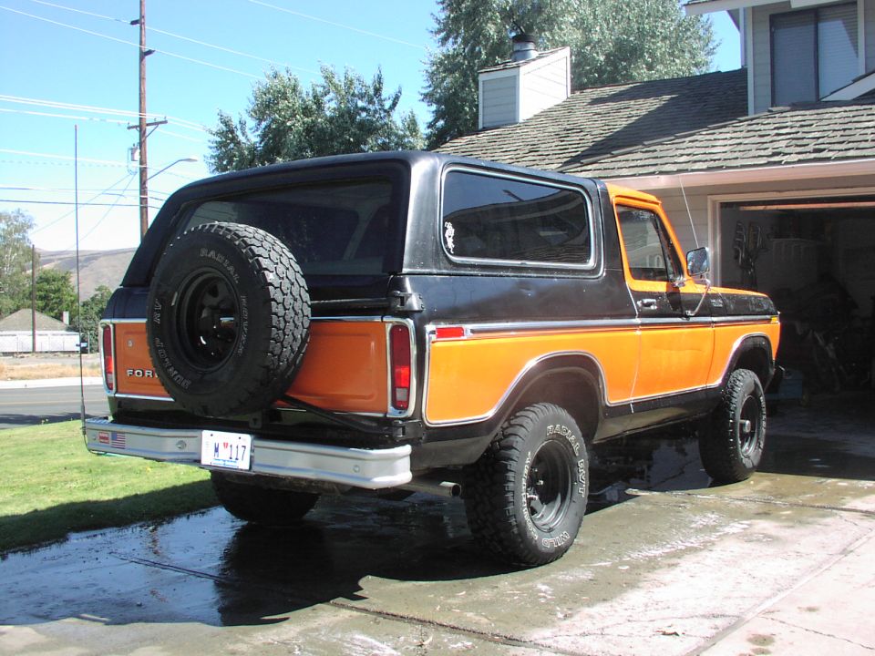 Rear view of an orange and black Ford Bronco with a spare tire mounted on the back. License plate reads W 117